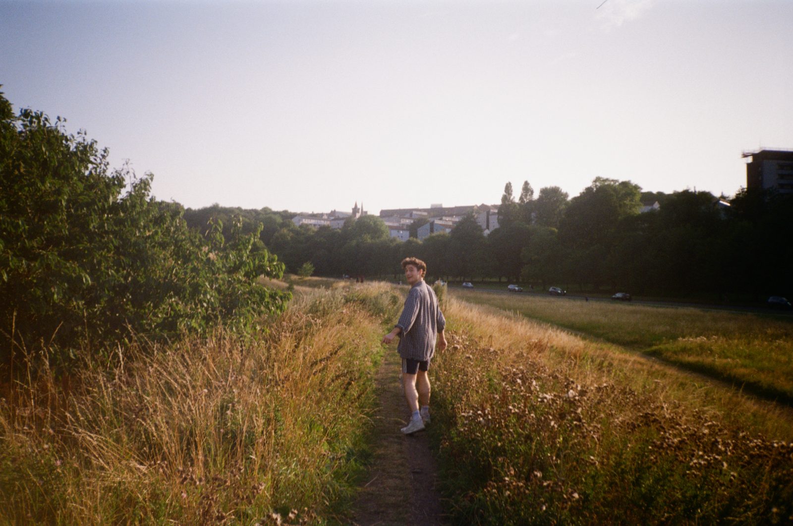 alex walking along a path through long grass, looking back
