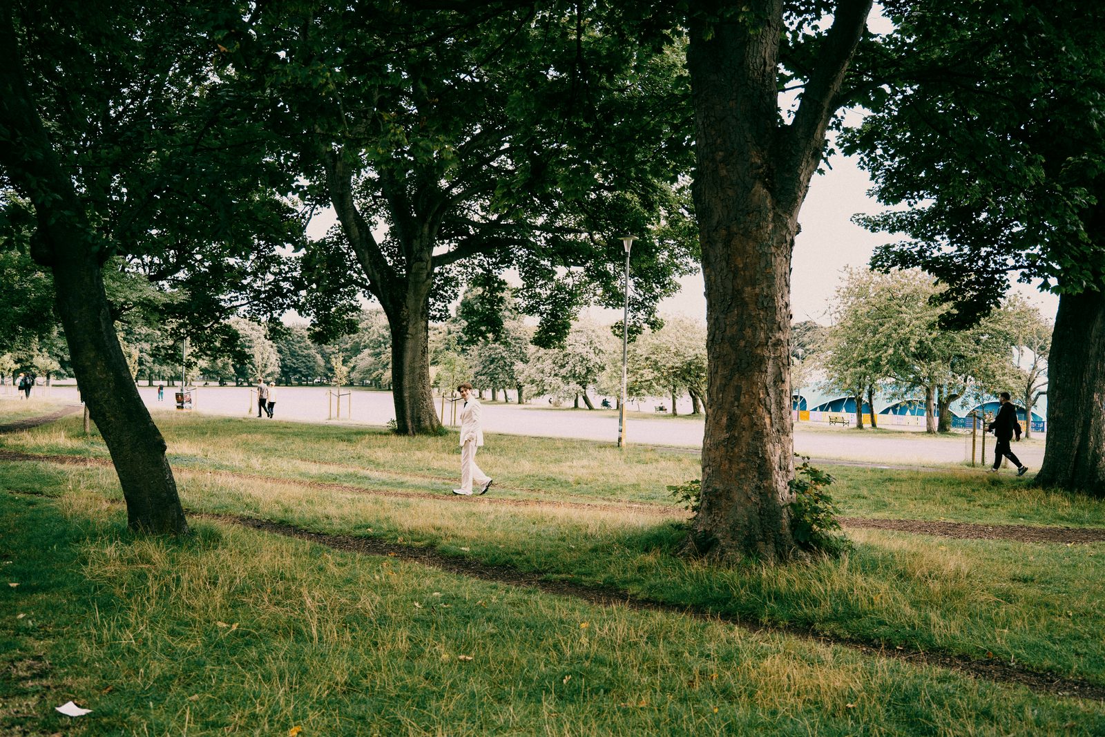 alex in a white suit walking through a park in edinburgh